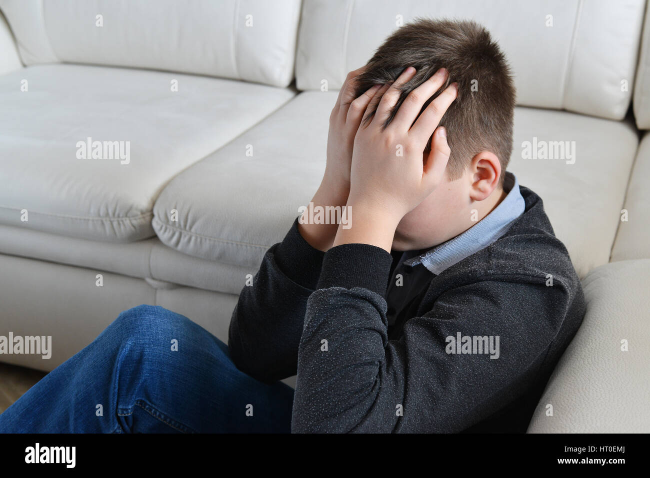 Upset teenager 13 years, he sits near sofa covering her face with her hands Stock Photo