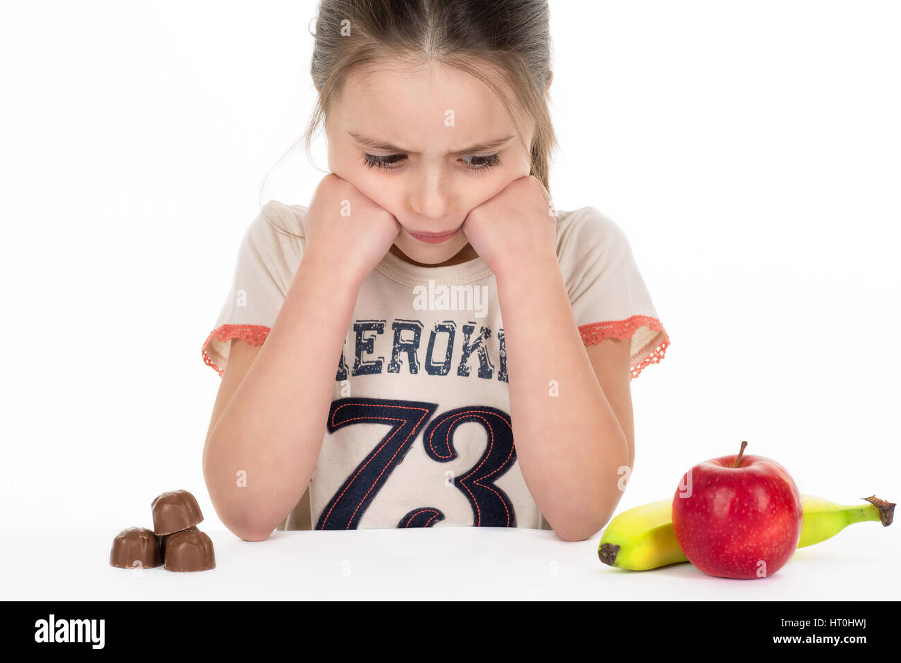 Girl deciding between sweets and fruits. Isolated. White background. Stock Photo