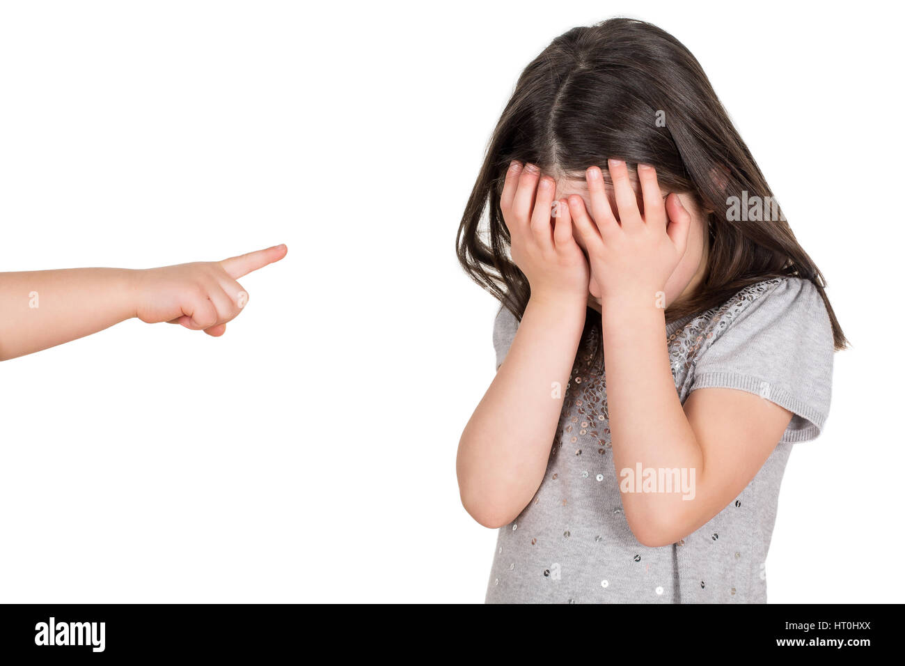 Crying school girl covering hear eyes being bullied. Finger pointing someone. Isolated on a white background. Stock Photo