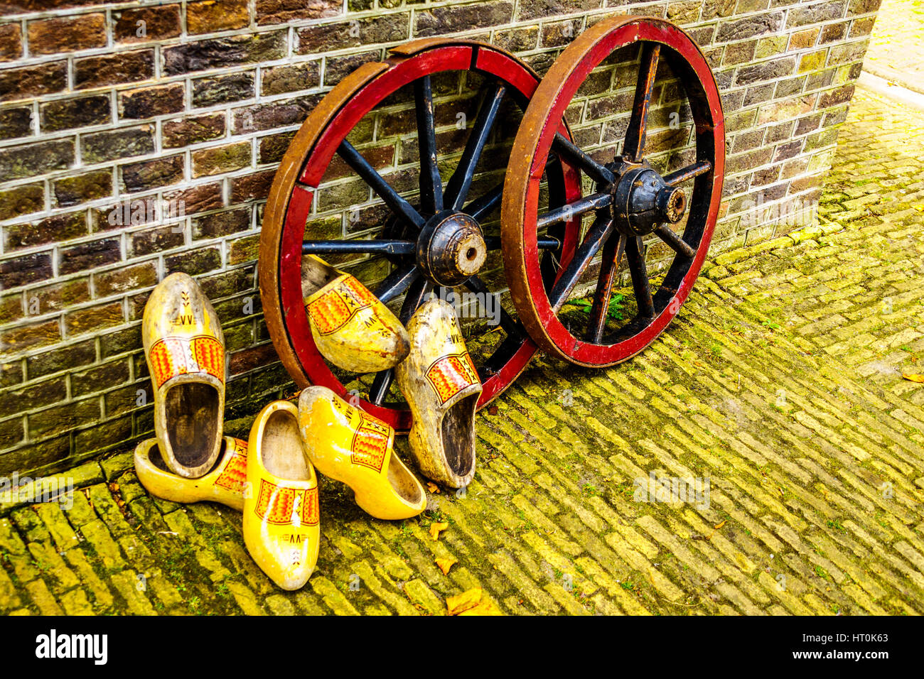 Old yellow painted Dutch Wooden Shoes resting against steel rimmed wooden Wagon Wheels with wooden spokes Stock Photo