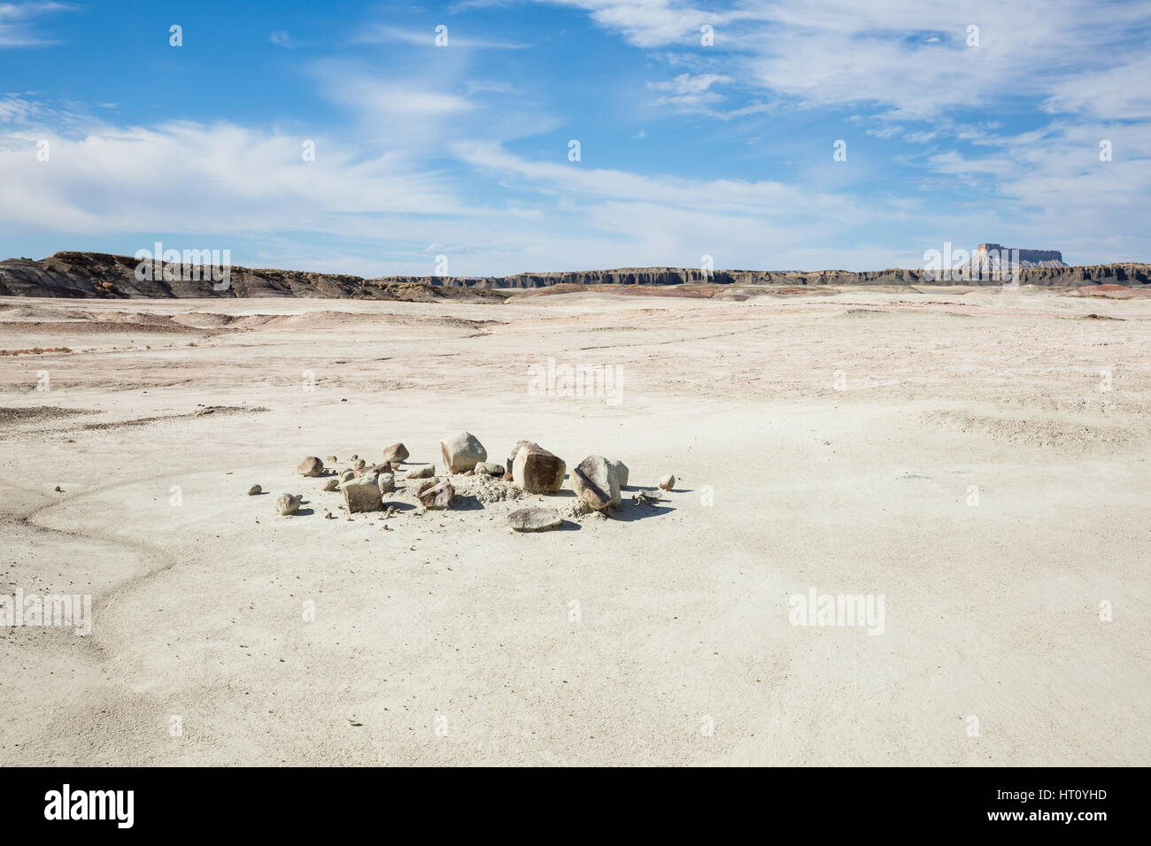 A desert scene with a large flat area of dirt and a broken boulder in a pile in the foreground. In the background are small brown hills and a large pl Stock Photo