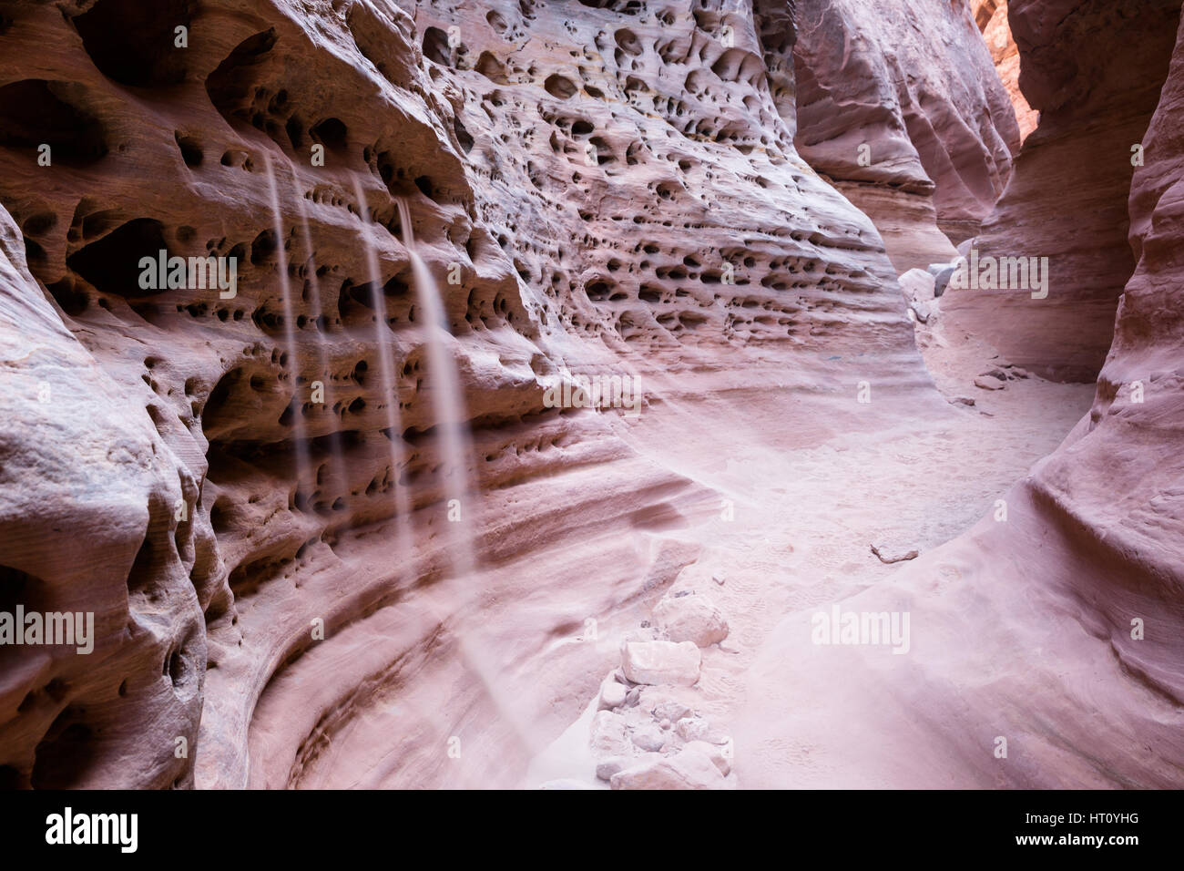 Sand placed in several small holes in the side of a slot canyon pours out to the sandy canyon floor. A long exposure smooths everything out for a soft Stock Photo