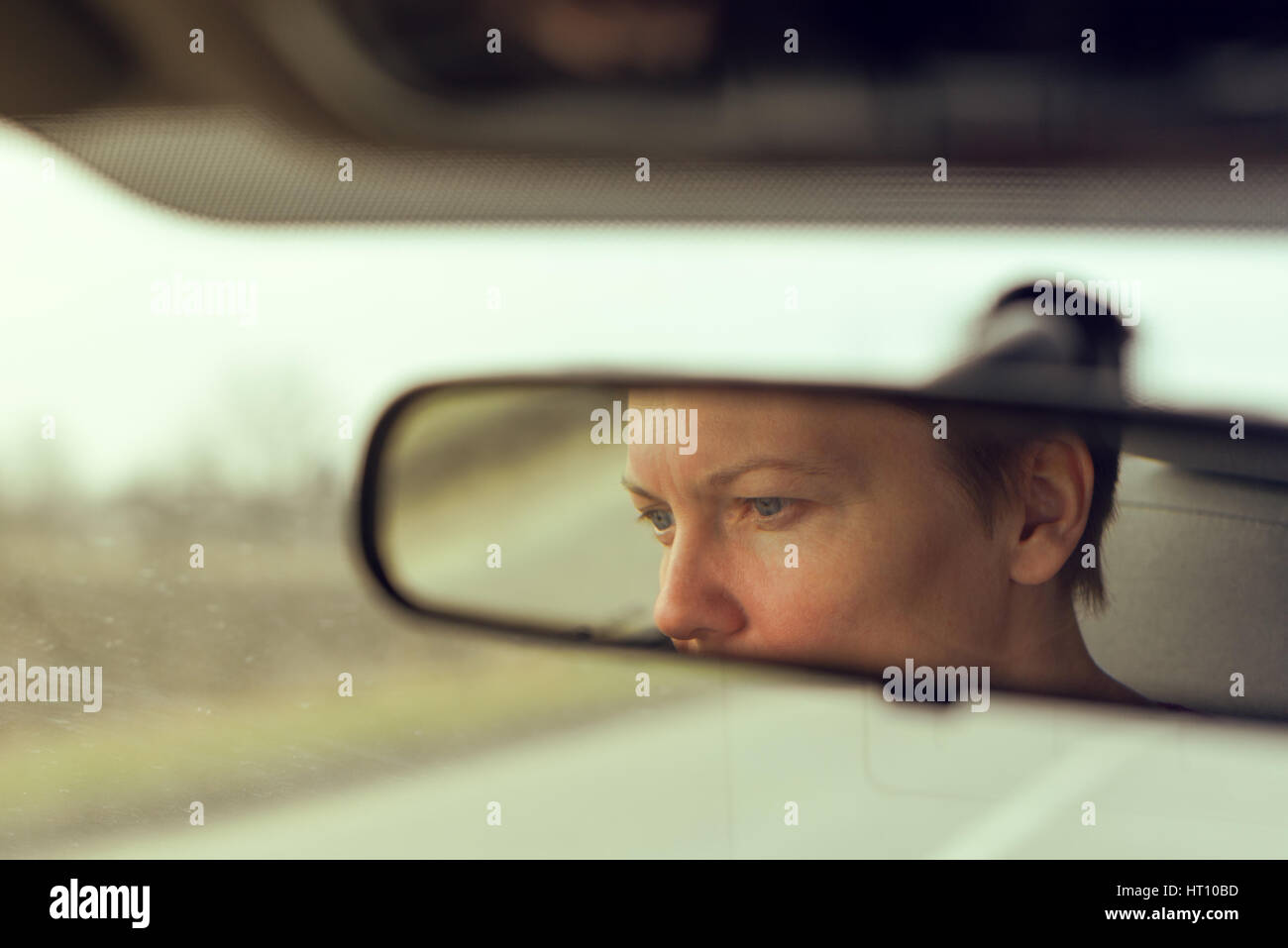 Reflection of female face in car rearview mirror while overtaking someone on open road, retro toned Stock Photo