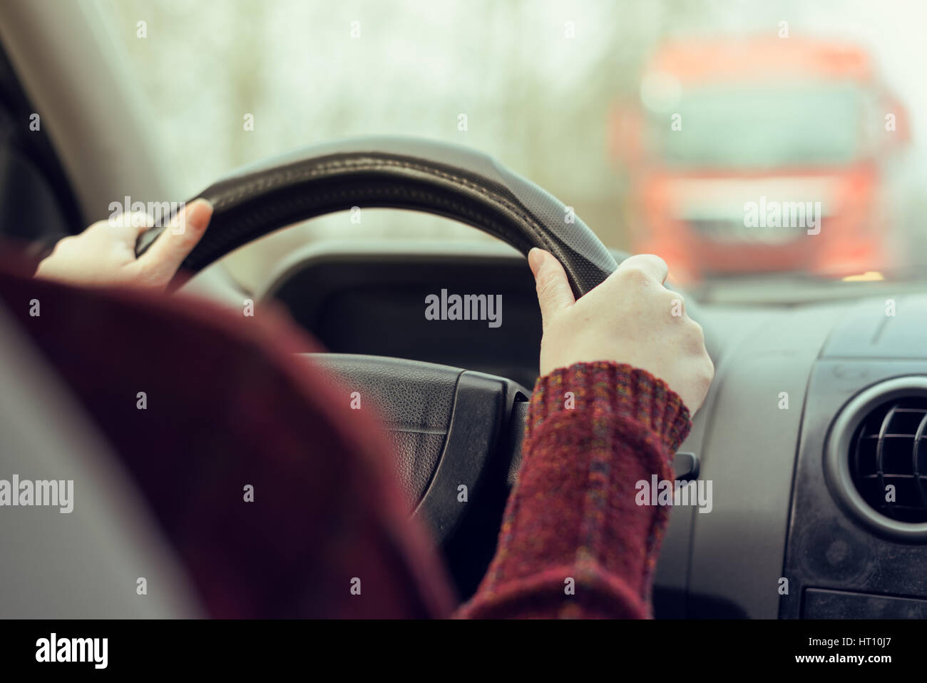 Woman driving car toward a large truck on the road, selective focus on hands gripping the steering wheel of the vehicle, retro toned image Stock Photo