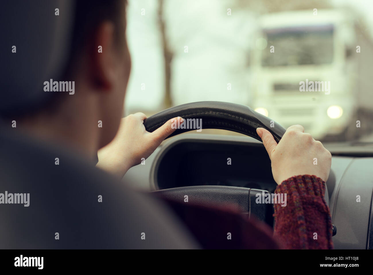 Woman driving car toward a large truck on the road, selective focus on hands gripping the steering wheel of the vehicle, retro toned image Stock Photo