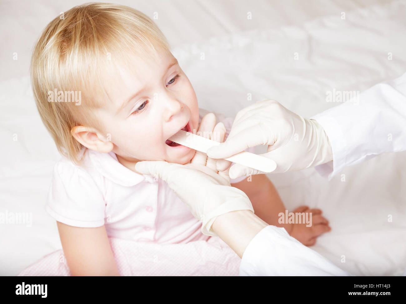 Pediatrician examines sitting child using wooden tongue depressor to