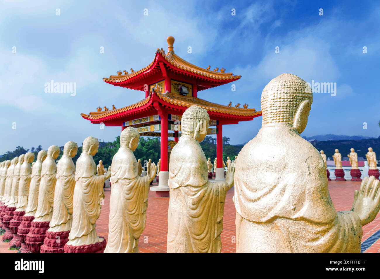 Row of golden Buddha statues with blurred temple in the background Stock Photo