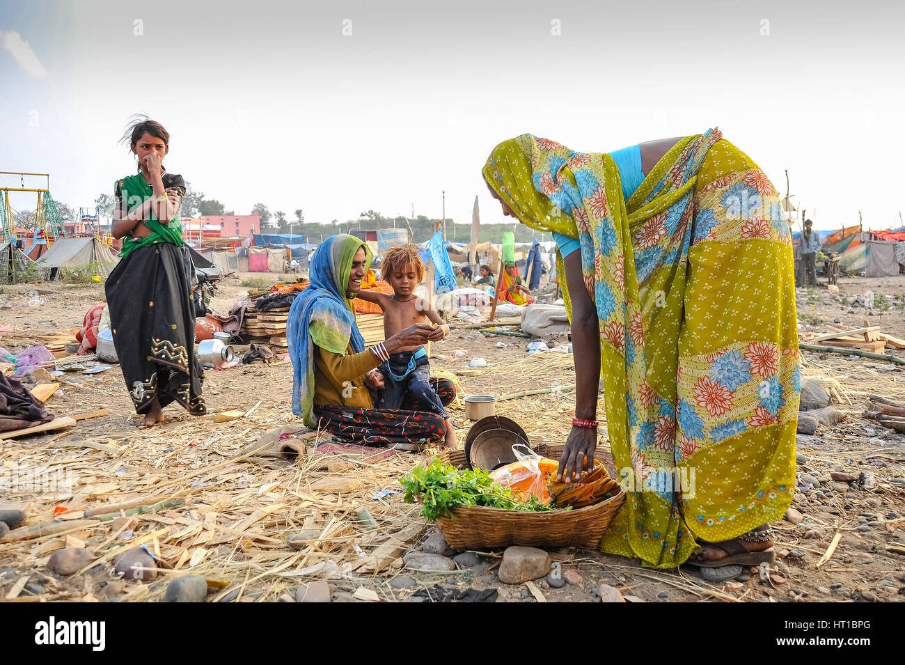 Women selling herbs and vegetables from a basket to a woman and children Stock Photo