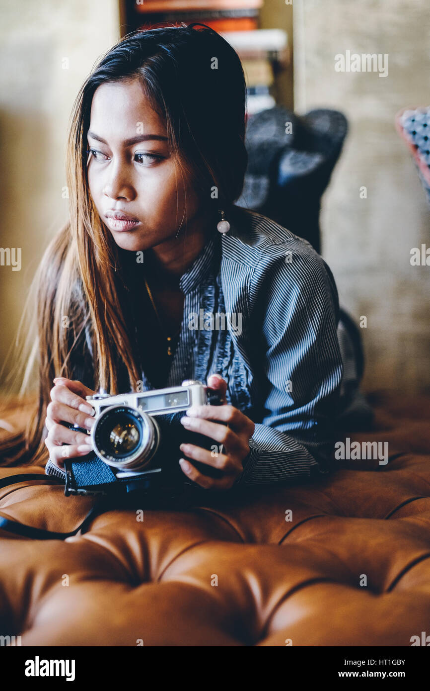 Hipster girl holding camera on leather sofa Stock Photo