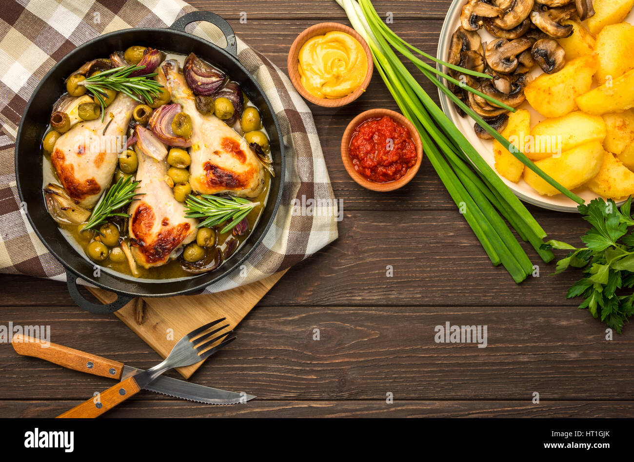 Dinner with baked chicken legs with olives spiced with aromatic herbs and potatoes with mushrooms on a rustic background. Top view, copy space. Stock Photo