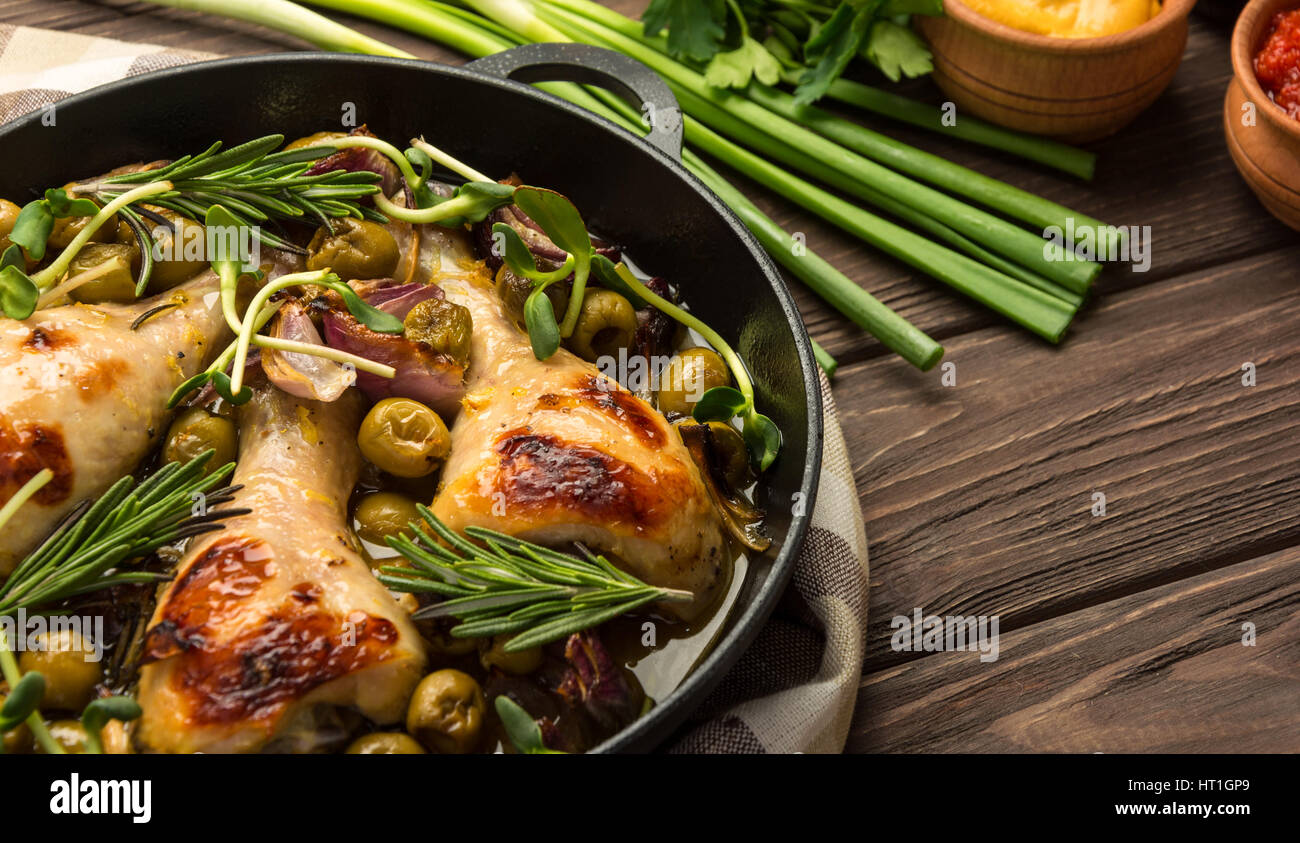 Baked chicken legs with olives spices and herbs on a rustic background. Copy space. Stock Photo