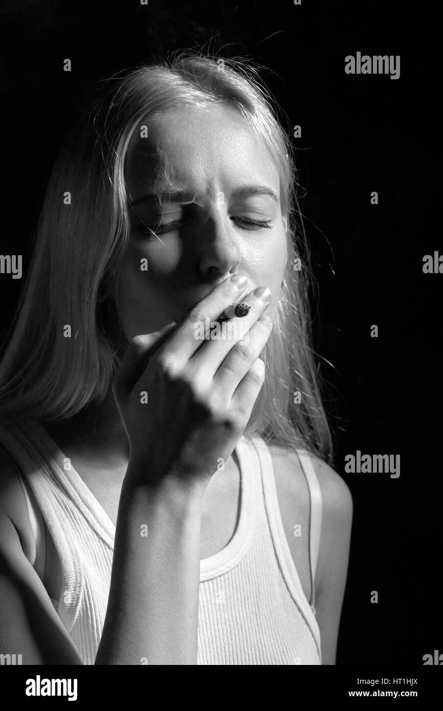 sad blond girl smoking joint with marijuana, monochrome Stock Photo