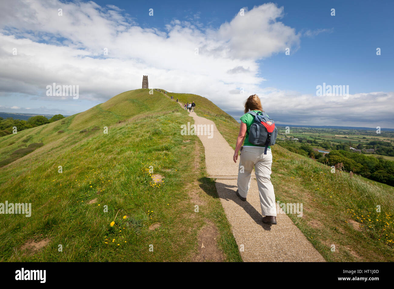 Glastonbury, United Kingdom - May 29, 2011: Rear view of a woman walking up the path on Glastonbury Tor towards St Michael's Tower. The trees and fiel Stock Photo