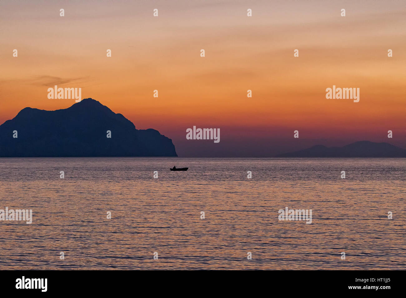 Small boat sunset silhouette is a fisherman's boat paddling along the water with a colorful purple and pink night sky in the background Stock Photo