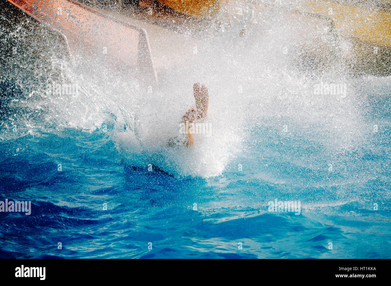 Caucasian adult falls into pool after going down water slide. Many water sprays, only the feet are visible. Summer vacation with water park concept. Stock Photo