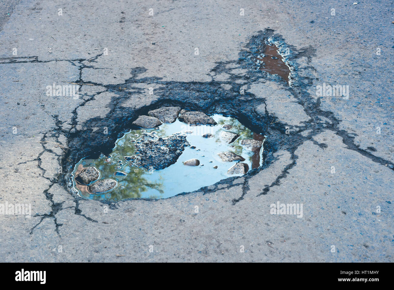 Large deep pothole with blue sky reflection and faded effect in Montreal street, Canada. Stock Photo