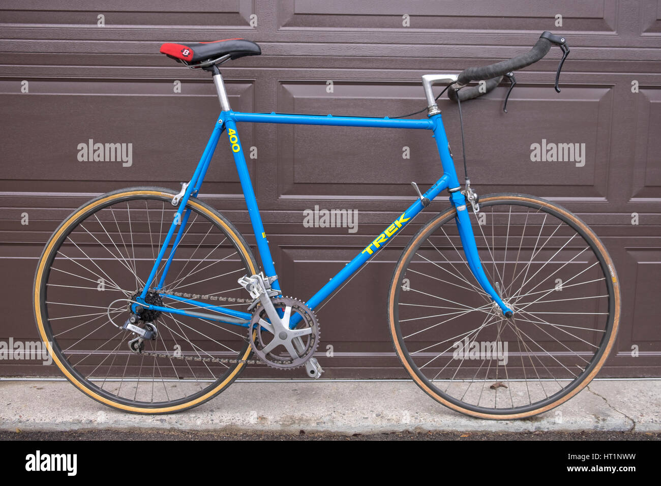 An old blue Trek 300 bicycle kitted out with bull horn handle bars leans against a brown garage door. Stock Photo