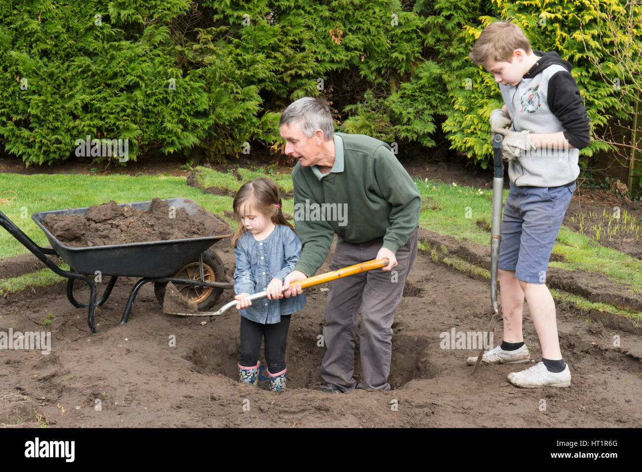 grandfather father with children digging wildlife pond in garden Stock Photo