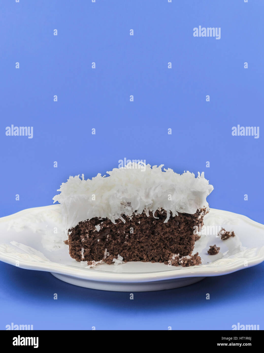 A piece of chocolate cake with fluffy white frosting topped with shreded coconut on a white serving plate. Oklahoma, USA. Stock Photo