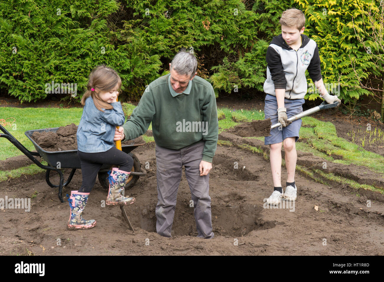 grandfather father with children digging wildlife pond in garden Stock Photo