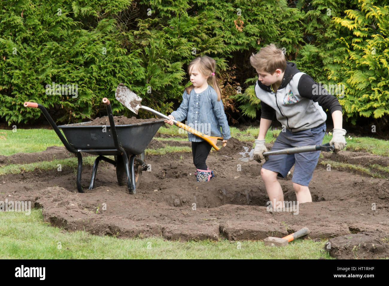 young girl and boy digging wildlife pond in garden Stock Photo