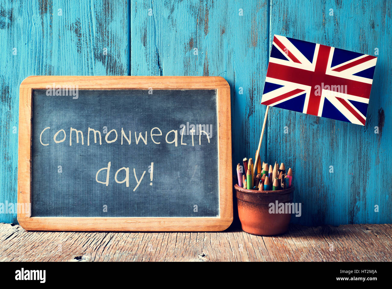 a wooden-framed chalkboard with the text commonwealth day written in it and the Union Flag in a pot of pencils, against a blue rustic wooden backgroun Stock Photo