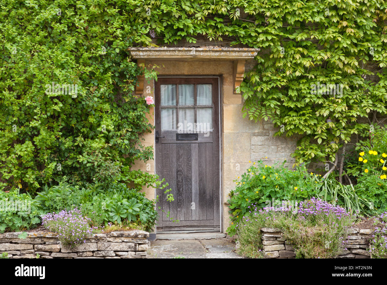 Old brown wooden doors in English stone house with flowers in the front ...