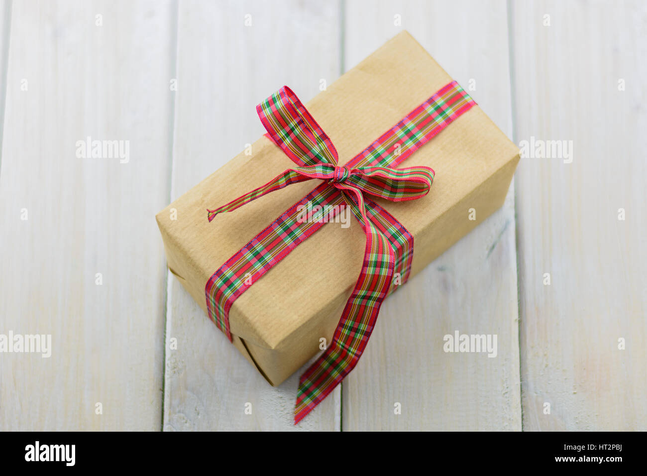 Box with a gift on a wooden table tied with red ribbon. Stock Photo