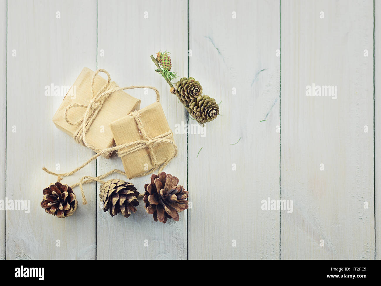 Two boxes with a gift on a wooden table tied with a rope decorated with a sprig of Christmas tree and pine cones. Stock Photo