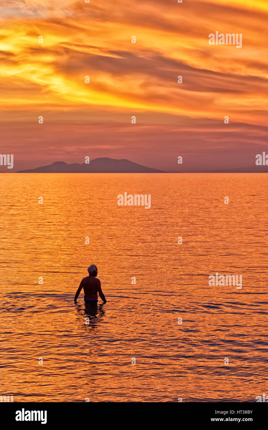 Silhouette of a Couple swimming in the sea against the backdrop of the sun setting on a beach with beautiful dramatic orange and red sky. Stock Photo