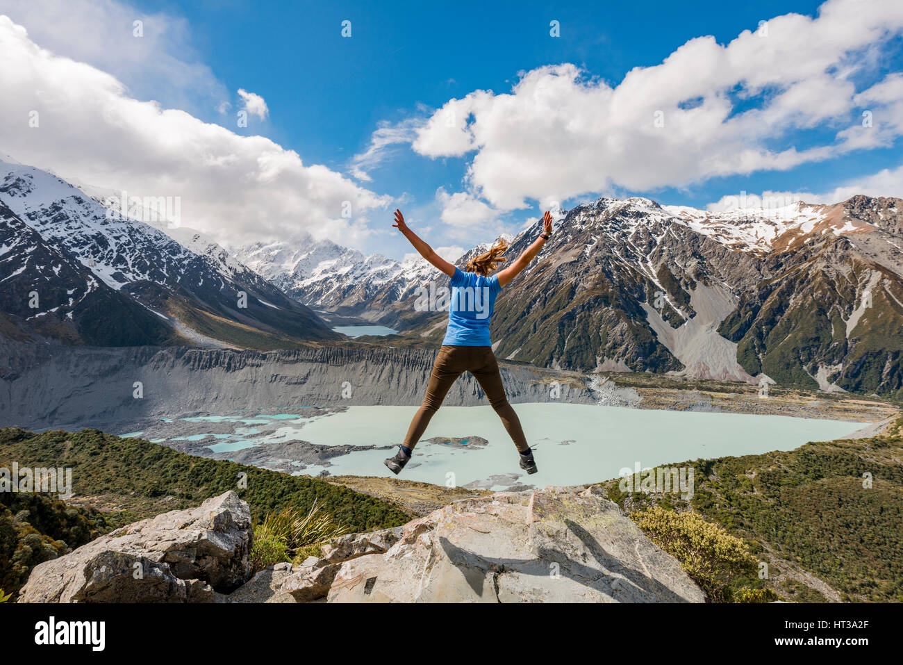 Hiker makes air jump, view into the Hooker Valley from Sealy Tarns Track, glacial lakes Mueller Lake and Hooker Lake Stock Photo