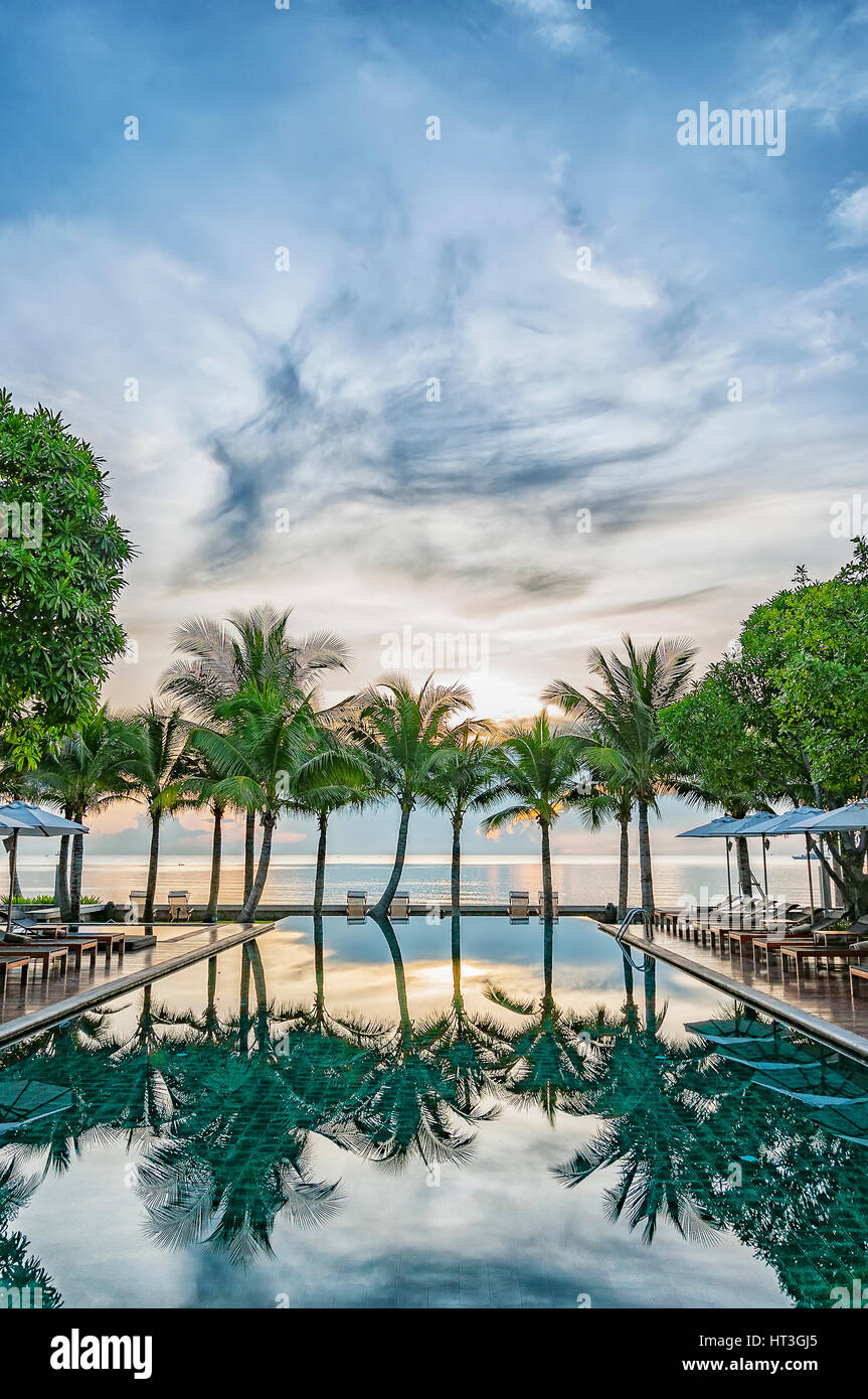A hotel infinity pool in Thailand at sunrise with a paradise backdrop of palm trees and ocean.. Stock Photo