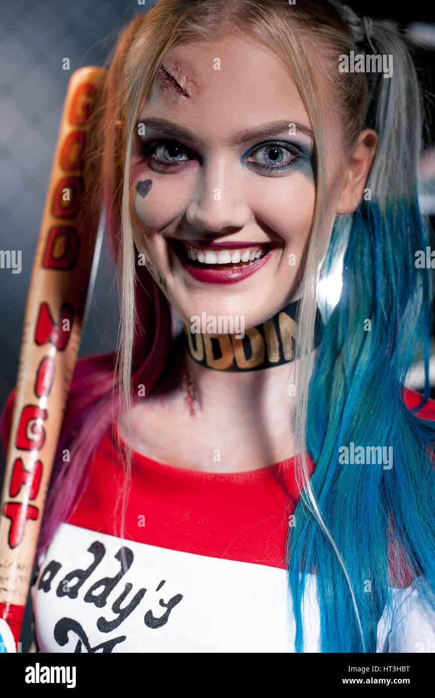 Portrait of smiling girl in costume Harley Quinn with crazy eyes. She stands with bat. Close up. Cosplay. Stock Photo