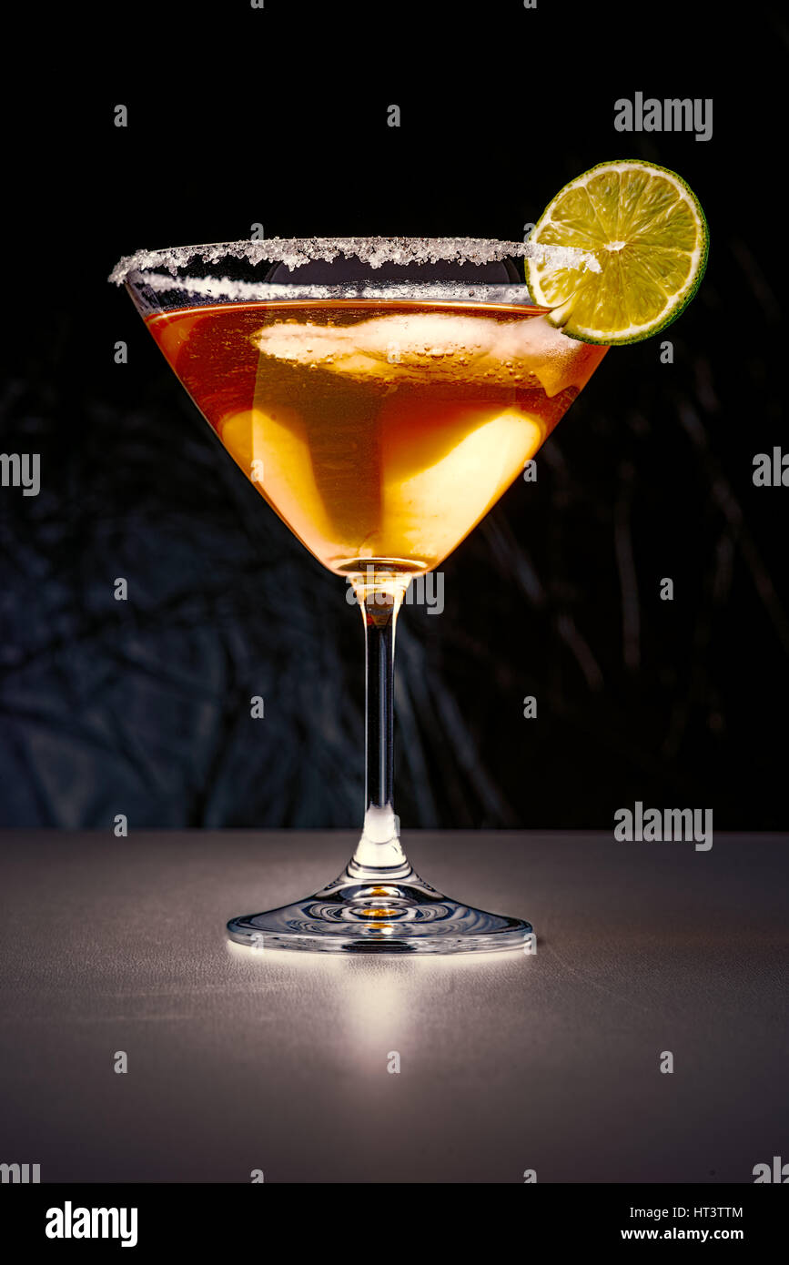 Martini glass with sugar edges, iced cocktail and lime slice in the dark Stock Photo