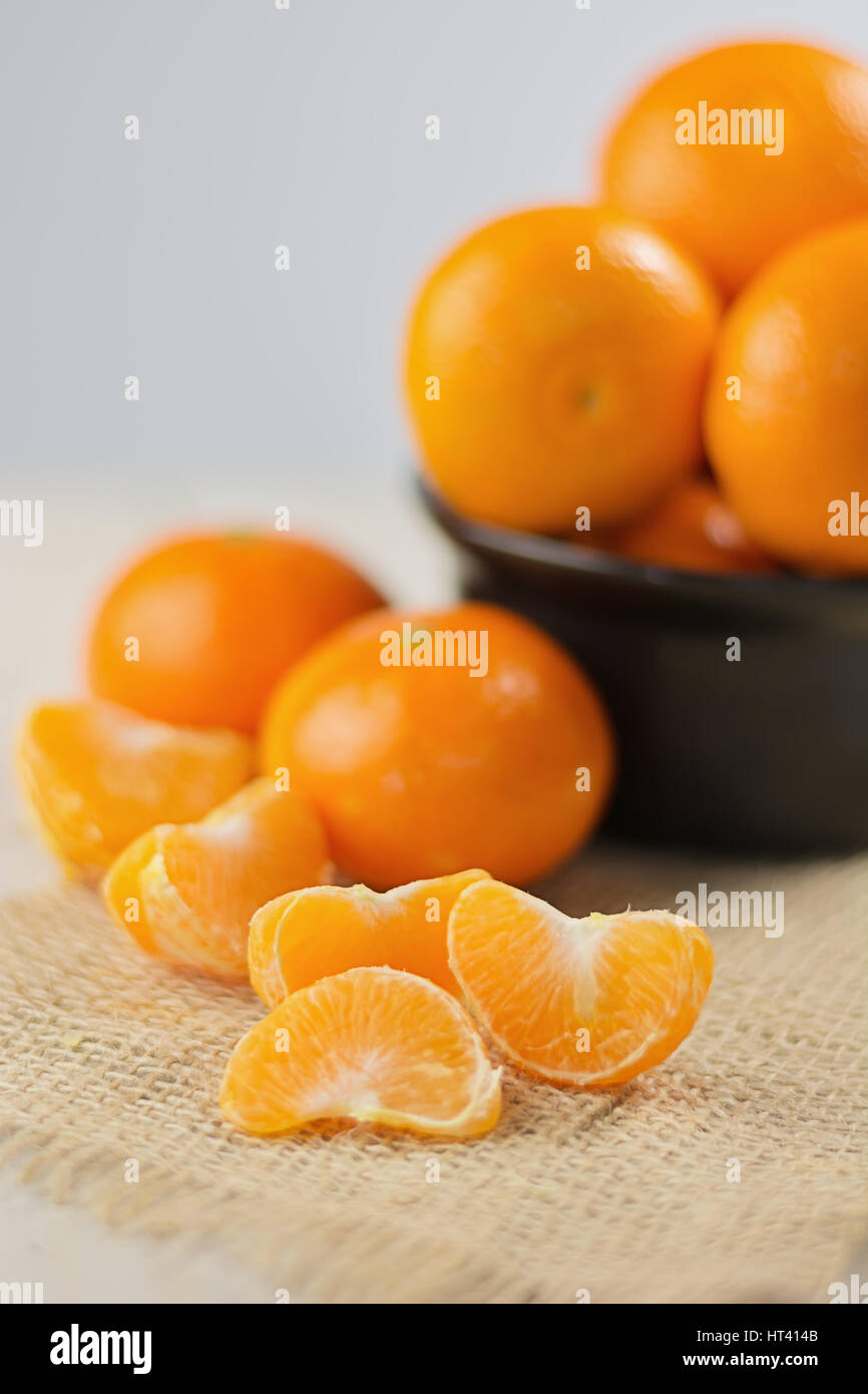 Group of tangerines in a small black bowl and peeled mandarin in the