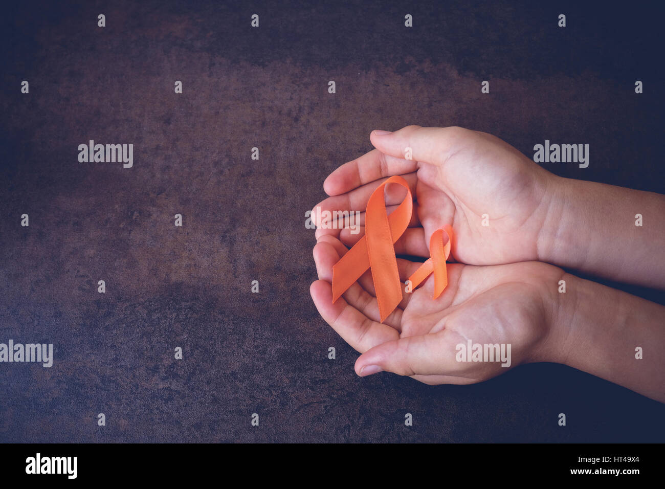 Hands holding Orange Ribbons on toning background, Leukemia awareness