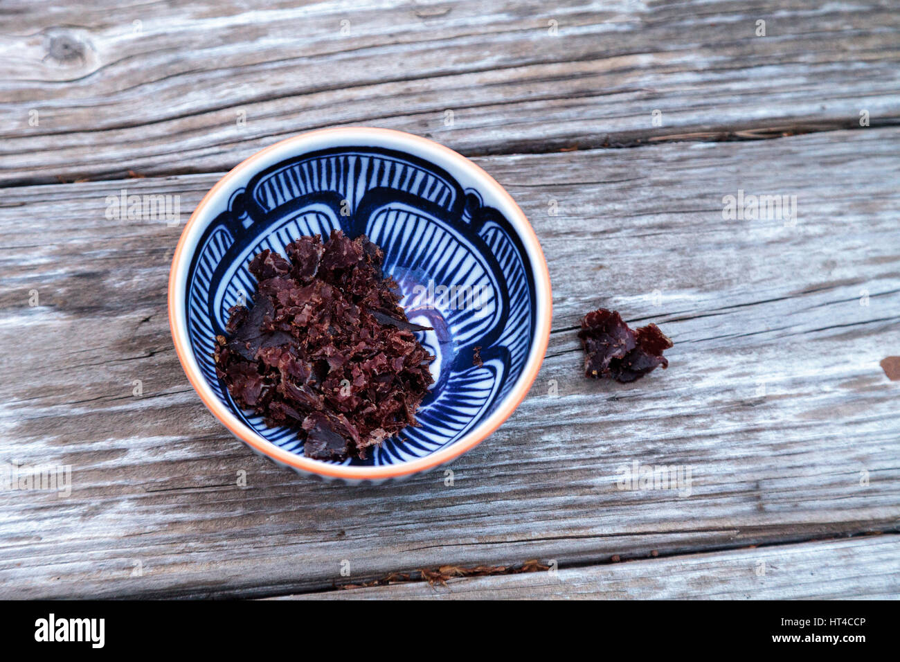 South African beef biltong, cured meat in a blue and white patterned bowl on a rustic wood table. Stock Photo