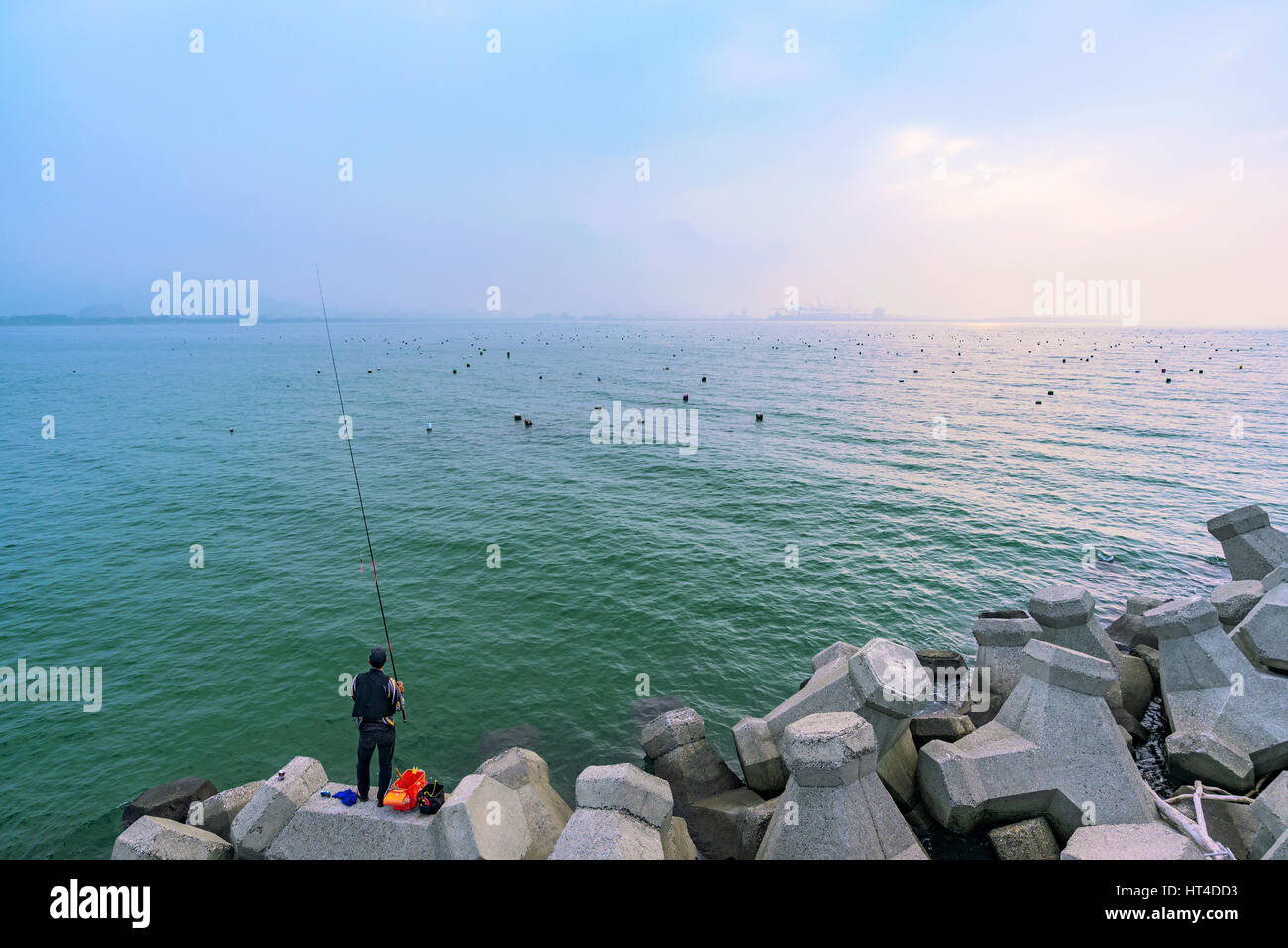 TAIPEI, TAIWAN - JANUARY 05: Fisherman  alone trying to catch fish along the rocky seafront in the Tamsui area of Taipei on January 05, 2017 in Taipei Stock Photo