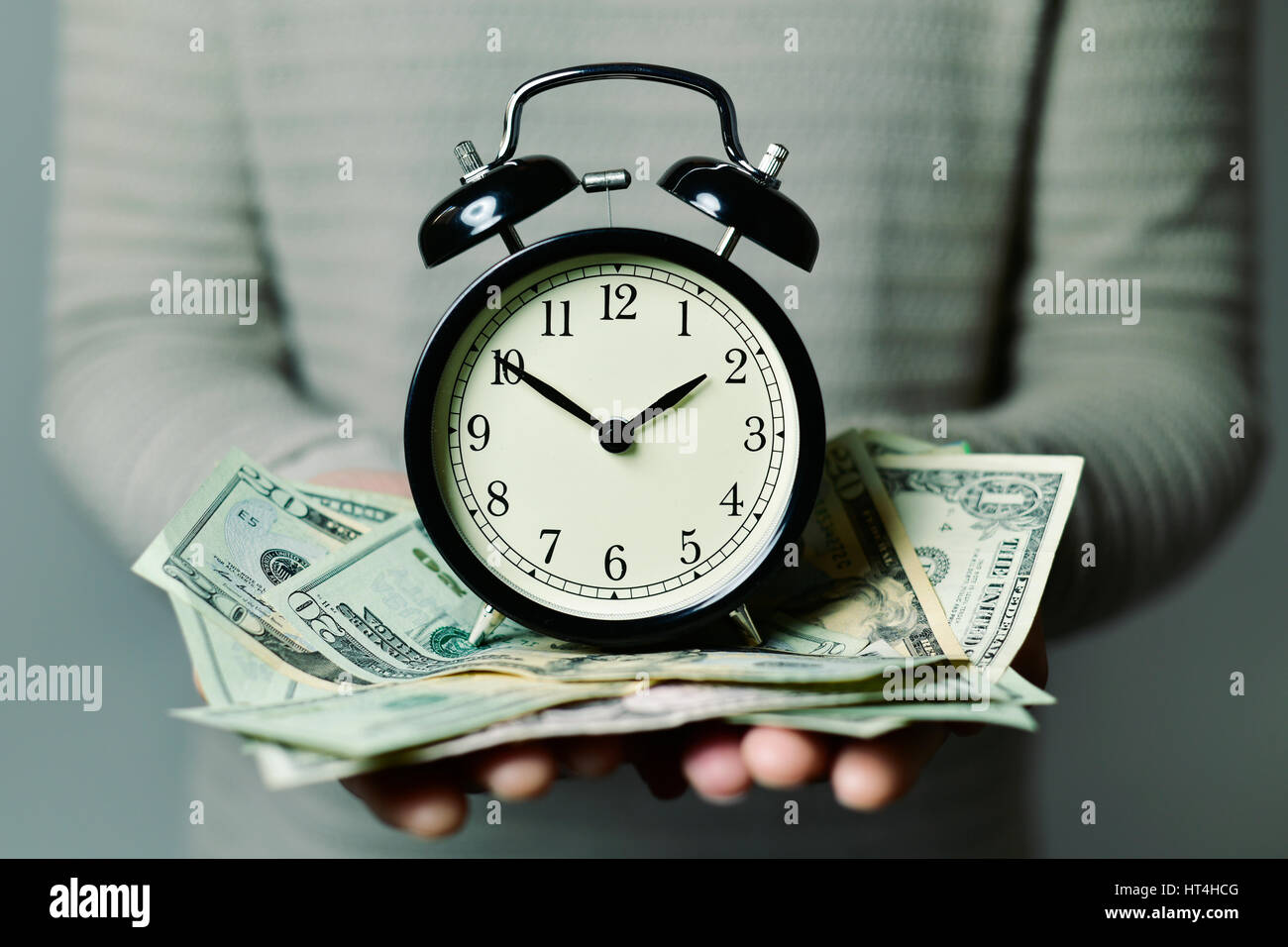 closeup of a young caucasian man with an alarm clock and many US dollar banknotes in his hands, depicting the idea that time is money Stock Photo
