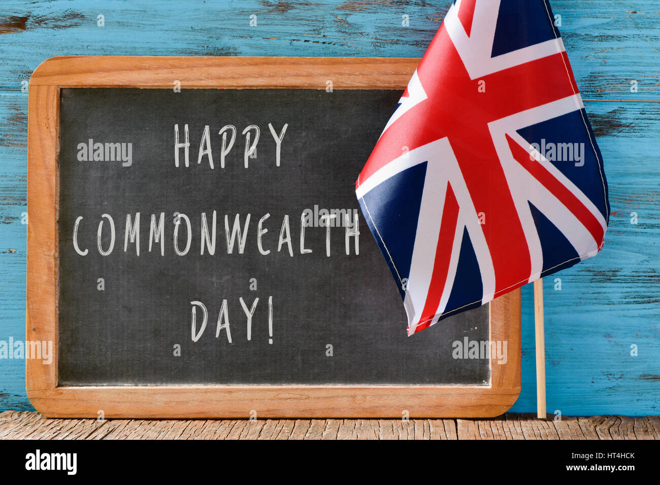 a wooden-framed chalkboard with the text happy commonwealth day written in it and the Union Flag against a blue rustic wooden background Stock Photo
