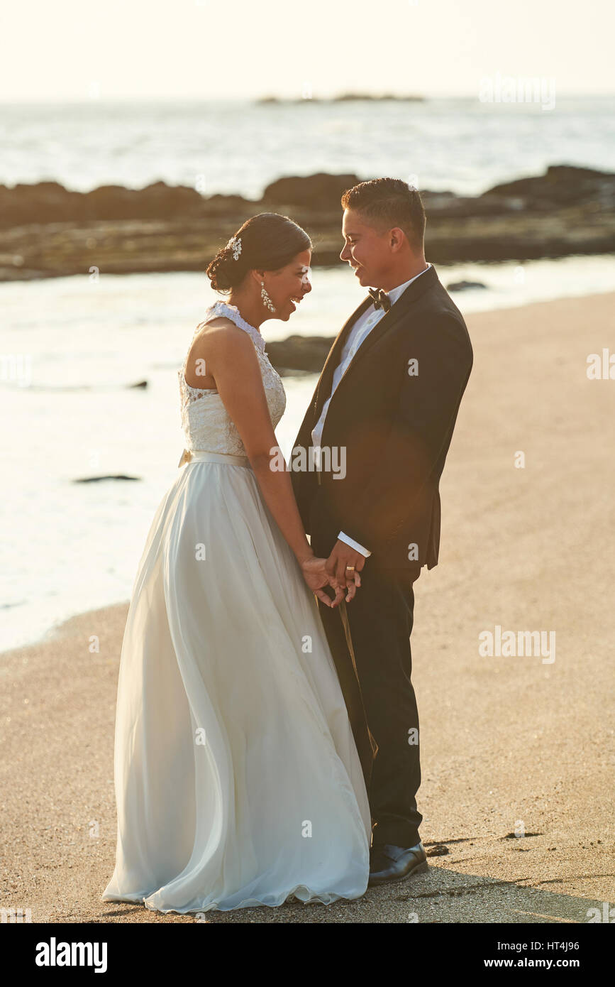 Happy married couple laughing in beach sunset time. Hispanic couple on wedding day Stock Photo