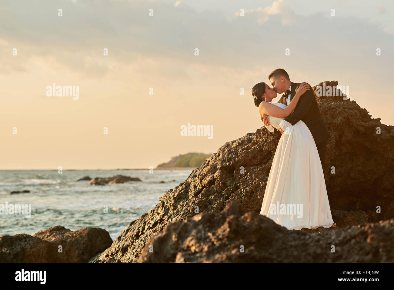 Bride and groom in love kissing on sun light ocean sunset background. Wedding on tropical exotic island Stock Photo