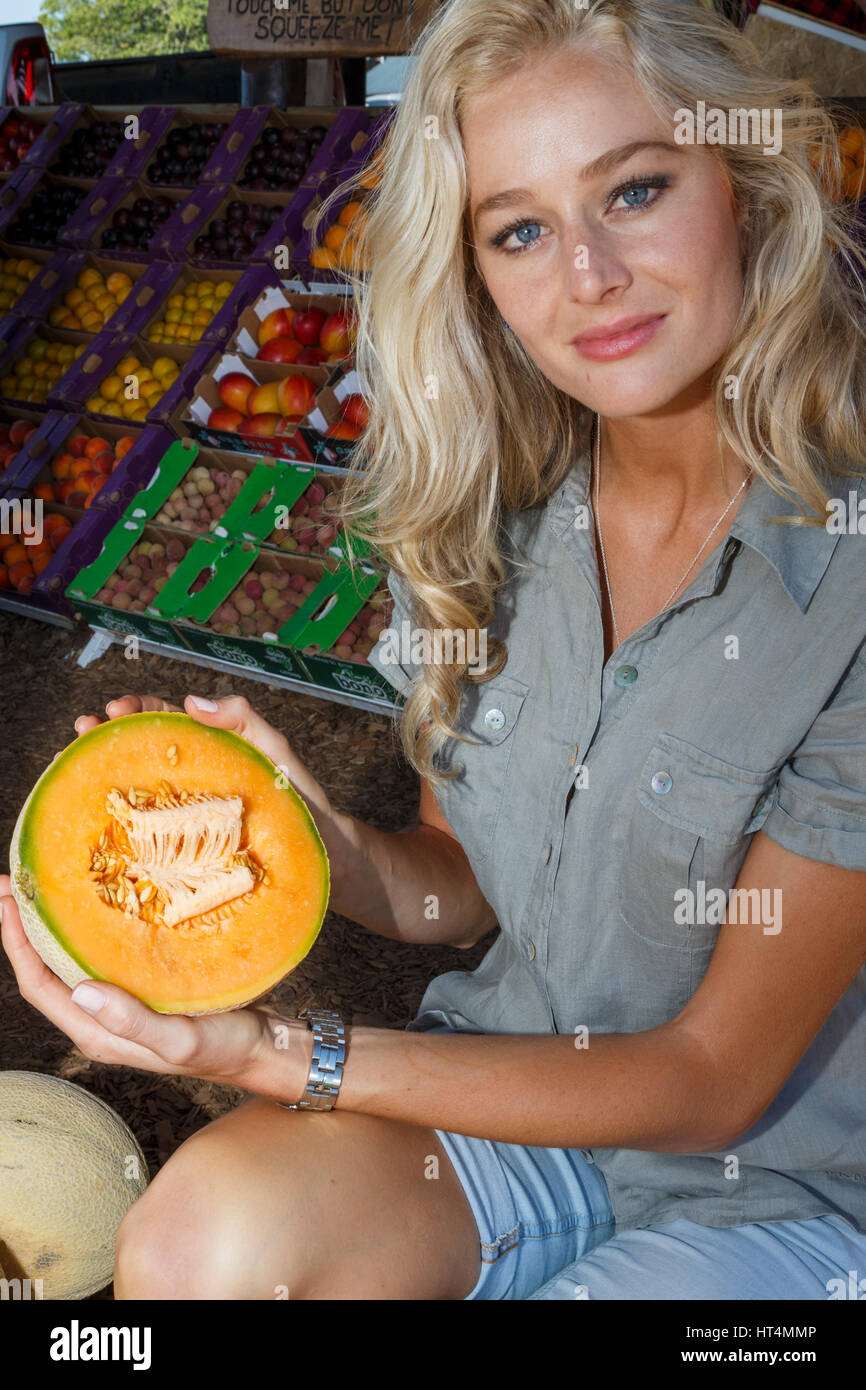 An attractive young long haired blonde adult woman buying fresh healthy and nutritious product at the farmers market. Stock Photo