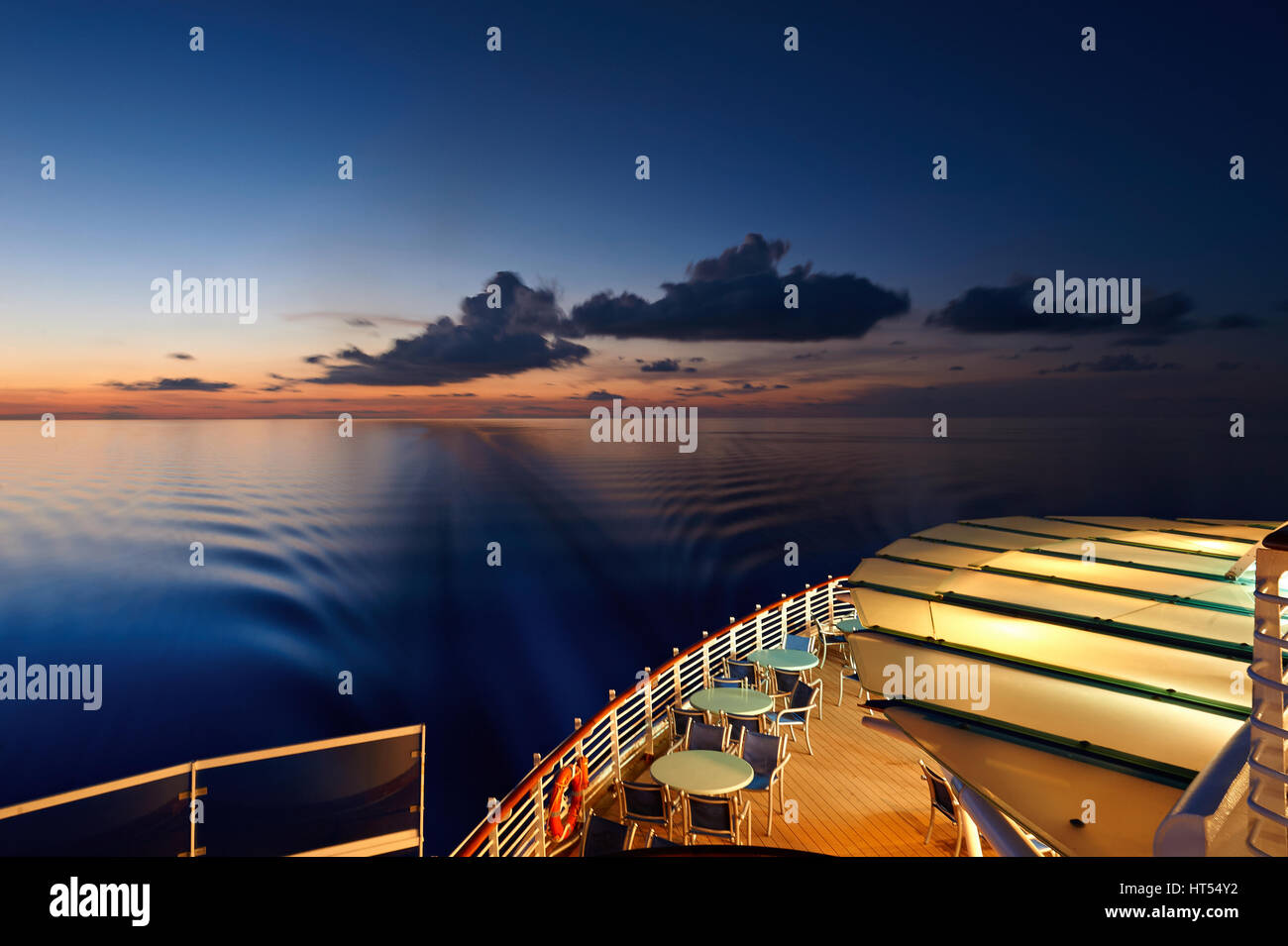 Back deck of cruise line ship with blurred trail on sea at sunset time. Tables on back deck Stock Photo