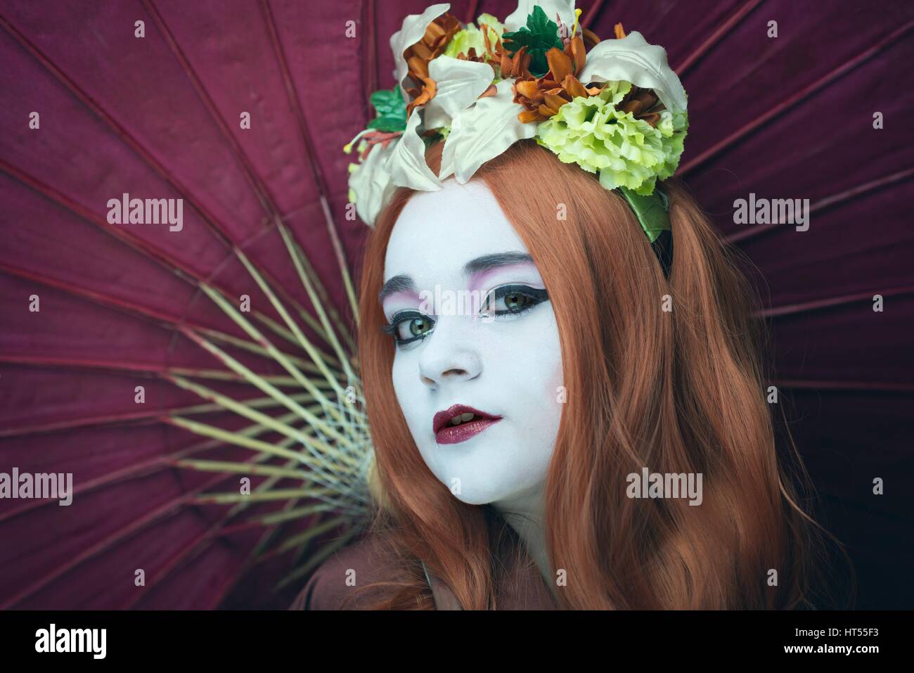 Woman dressed as a Geisha girl with parasol and floral garland in her hair Stock Photo