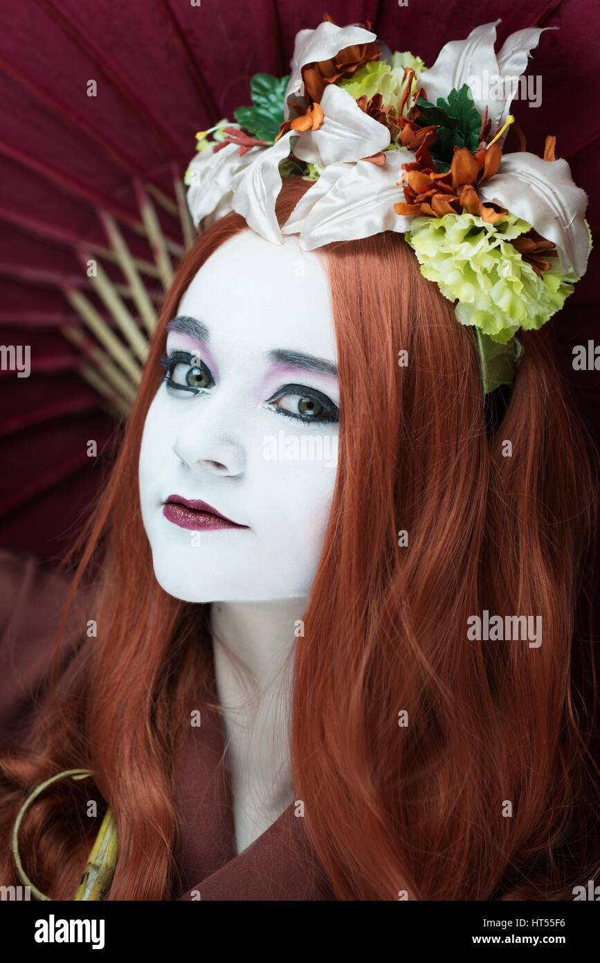 Woman dressed as a Geisha girl with parasol and floral garland in her hair Stock Photo