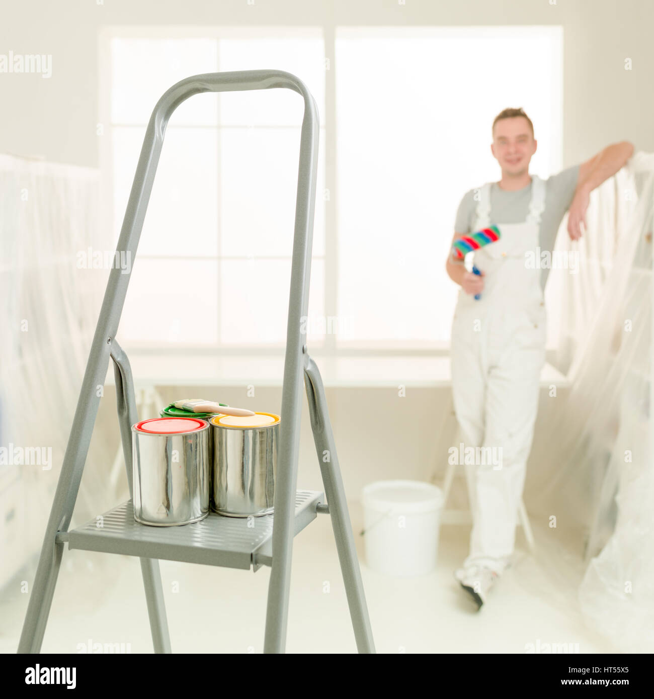 Square image colourful cans of paint on a stepladder young decorator in background blurred diy Stock Photo