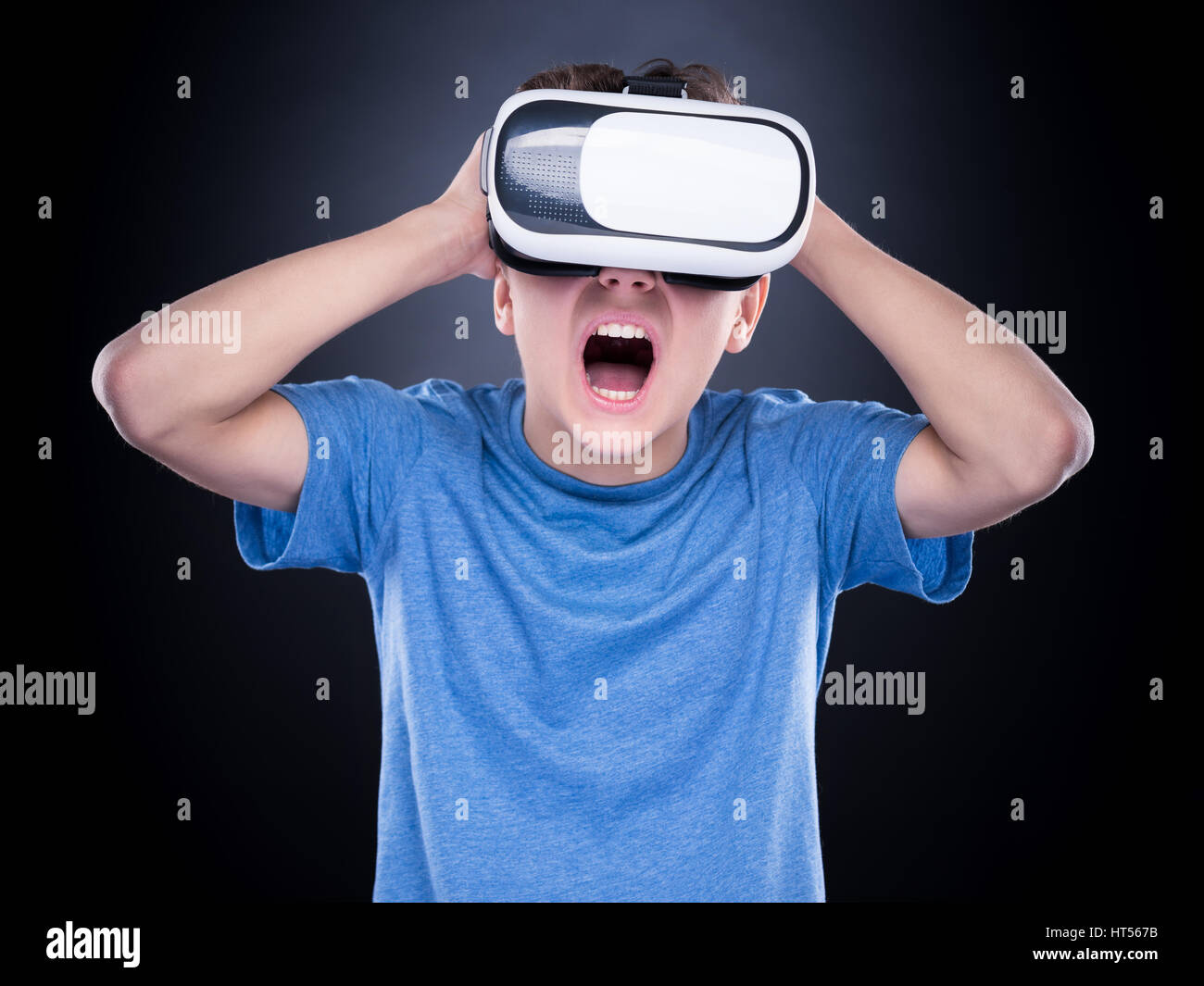 Amazed teen boy screaming, wearing virtual reality goggles watching movies or playing video games. Surprised teenager looking in VR glasses and shouti Stock Photo