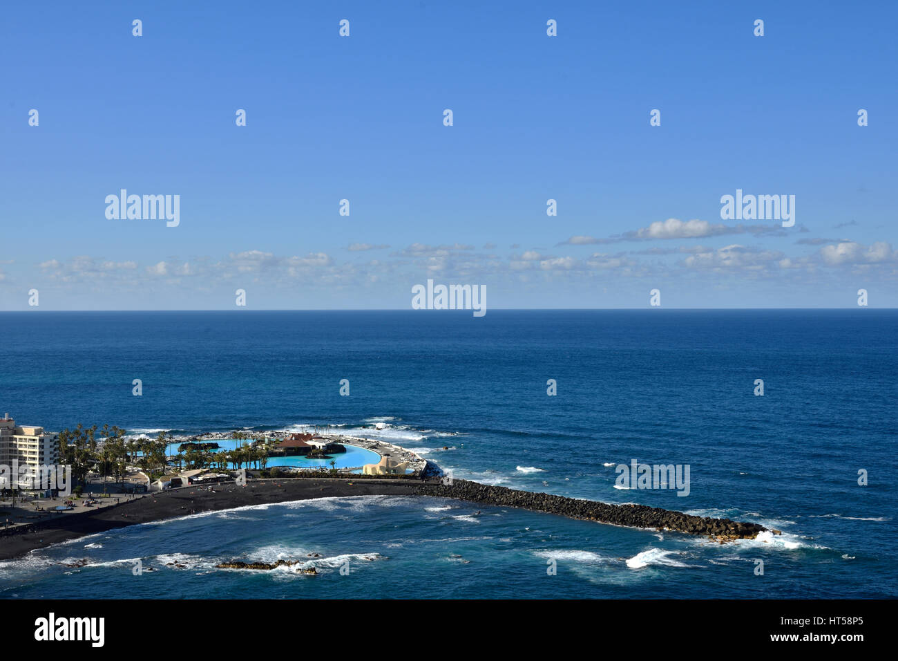 Resort and a beach with black lava sand and a pir as protection against waves,horizon and blue sky in background, picture from Puerto de la Cruz Tener Stock Photo