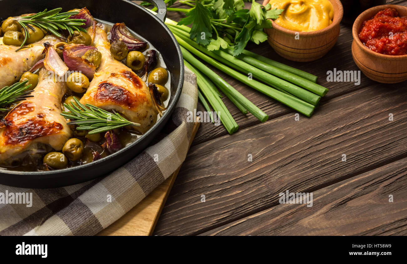 Baked chicken legs with olives spices and herbs on a rustic background. Copy space. Stock Photo